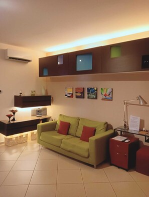 A living room with a green sofa, a red cabinet, and a wall-mounted air conditioner.