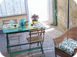 An outdoor dining area with a green table, chairs, and a wicker chair with a cushion.