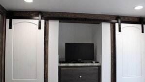 A room with a sliding door, a flat-screen TV on a stand, and a dark wooden dresser. - Coast Oak -Beautiful New Tiny Cottage - Perfect Family Getaway (Aransas Pass)