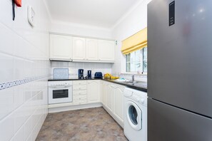 A modern kitchen with white cabinets, a stainless steel refrigerator, a washing machine, and a coffee maker.