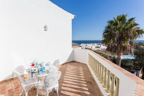 Een balkon met een witte tafel en stoelen, een betegelde vloer, en uitzicht op zee en gebouwen.