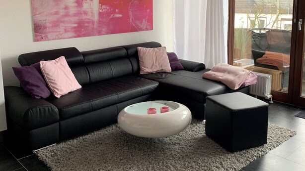 A modern living room with a black leather sofa, a white ottoman, and a large abstract painting on the wall. - Central apartment in Willingen (Willingen (Upland))