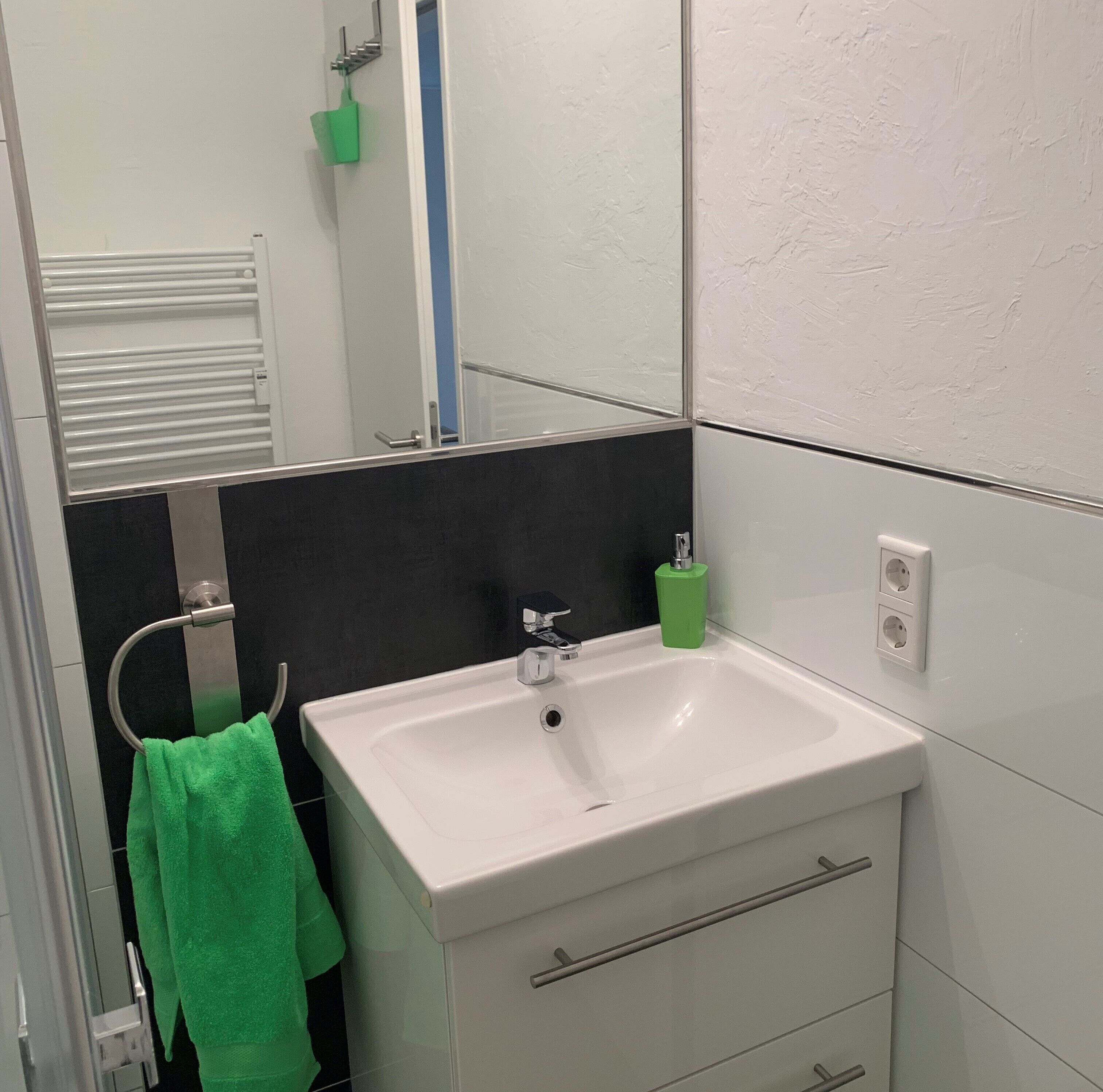 A bathroom with a white sink, a mirror, a towel rack with a green towel, and a black tiled wall.