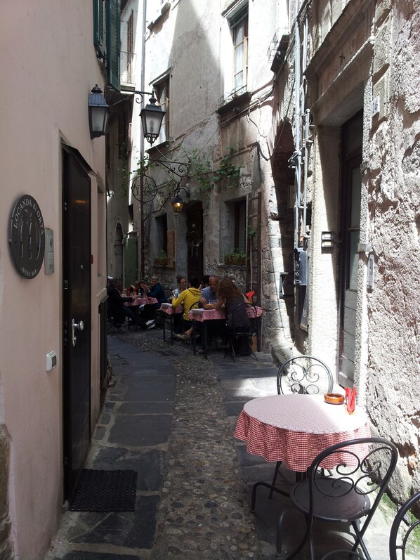 A narrow street with outdoor seating, stone walls, and a vintage atmosphere.