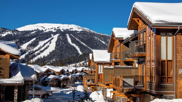Une station de montagne enneigée, avec des bâtiments en bois et une piste de ski en arrière-plan.