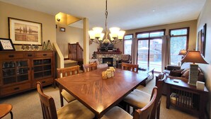 Un espace repas comprenant une grande table en bois, des chaises, un lustre et une cheminée.