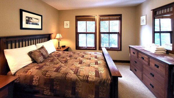 A bedroom with a large bed, a dresser, two windows, and a nightstand with a lamp. - Incredible multi level 2 bedroom + den townhouse, close to ski run (Sun Peaks)