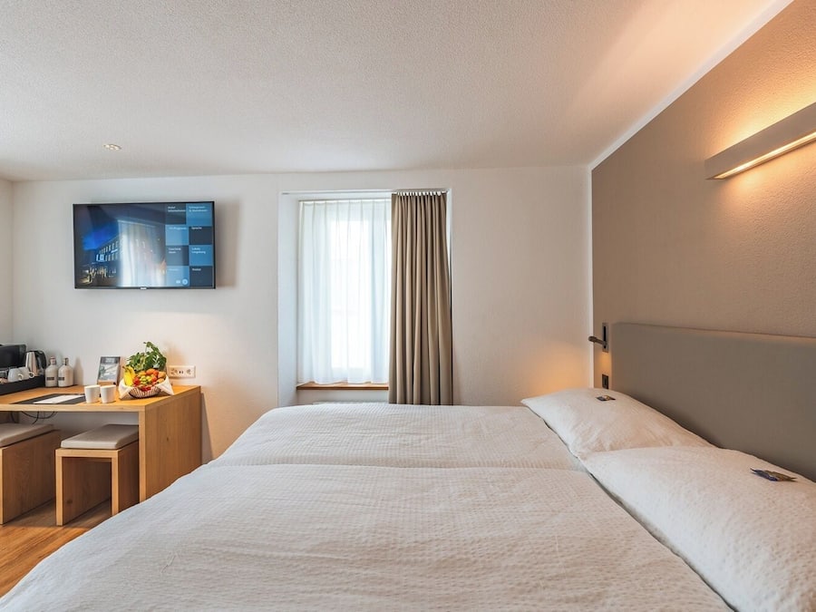 A hotel room with a large bed, a desk with a computer, a flat-screen TV, and a window with curtains.