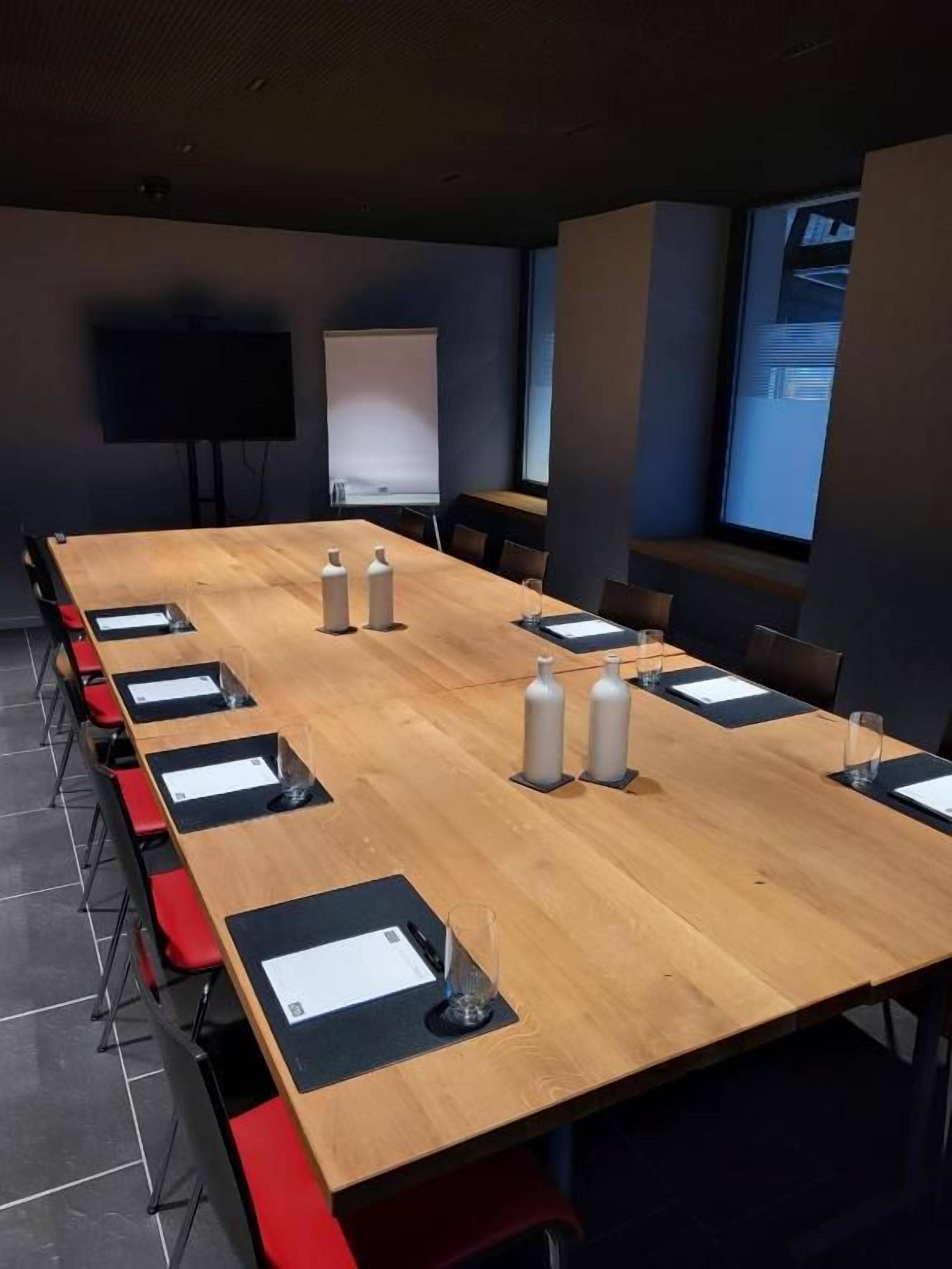 Un salón de conferencias con una larga mesa, sillas, una pantalla de proyector y una pizarra.