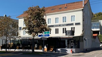 Un hotel llamado 'Hotel Artist', con un letrero visible, una entrada clara y una señal de calle que indica lugares cercanos.