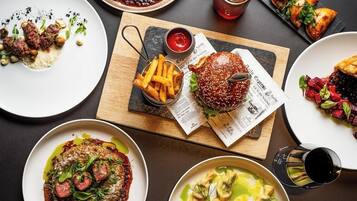 A variety of dishes including steak, burgers, and salads, arranged on a table with a newspaper.
