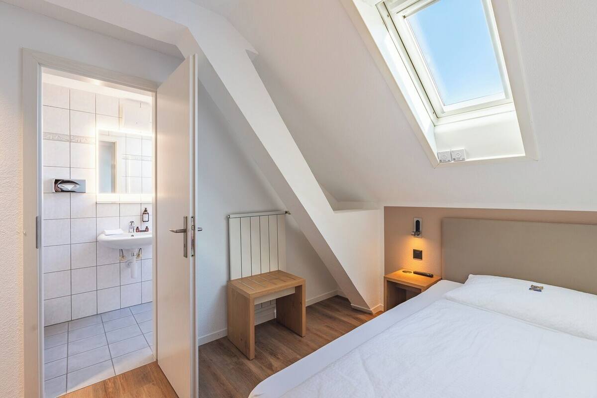 A bedroom with a skylight, a bedside table, a nightstand, and a bed.