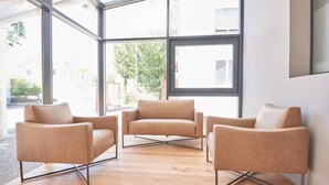 A modern interior with three leather armchairs arranged around a wooden floor, large windows offering a view of the outside. - Hotel Artist (Biel)