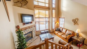 A cozy living room with a fireplace, leather sofa, and a flat-screen TV mounted on the wall.