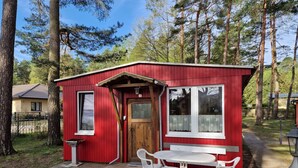 Eine kleine rote Holzhütte mit einer Holztür, einem Fenster und einem Tisch mit Stühlen davor.