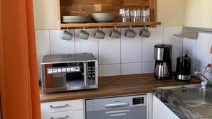 Eine kleine Küche mit Mikrowelle, Kaffeemaschine und eingebautem Backofen. Darüber befinden sich Regale mit Tellern und Gläsern.