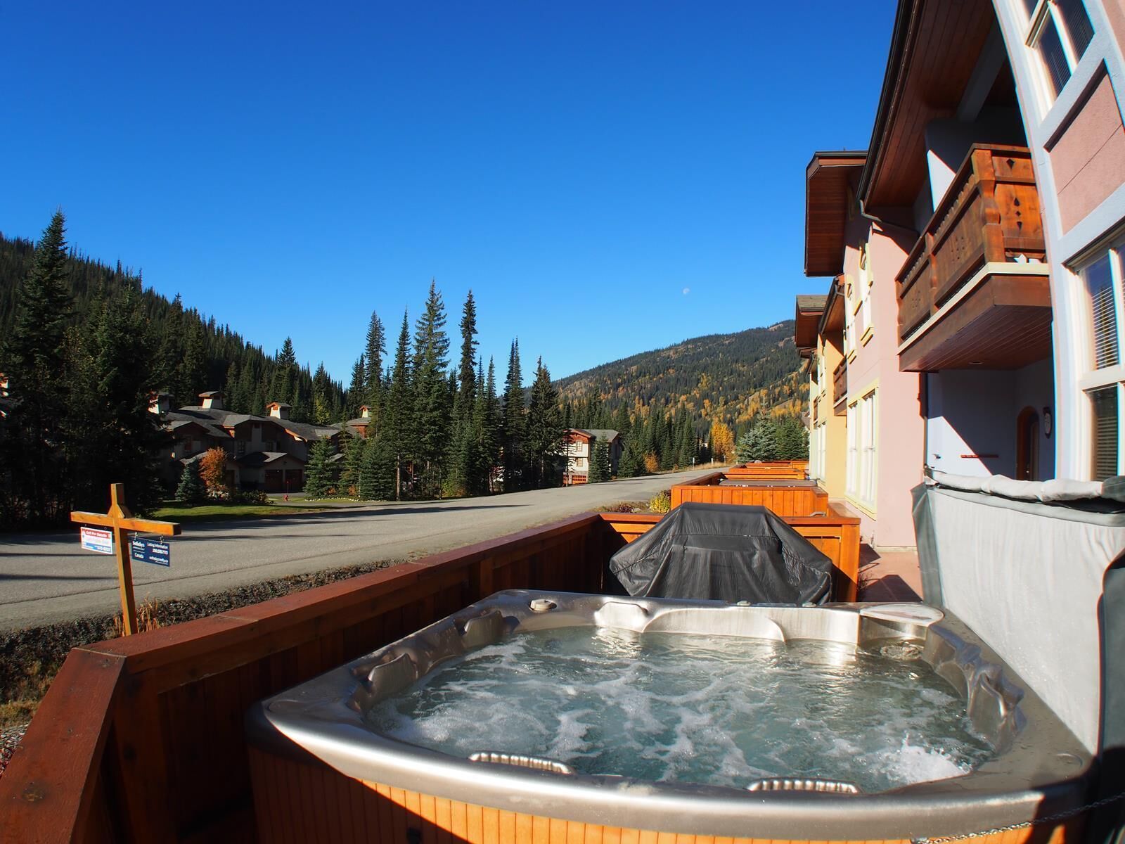 Ein Whirlpool auf einer Holzterrasse mit Blick auf einen Berg und ein Gebäude im Hintergrund.