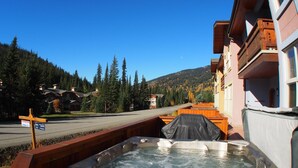 Una vasca idromassaggio su un pontile in legno, con vista su una montagna e un edificio sullo sfondo.