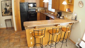 Una cucina con isola centrale, sgabelli da bar, mobili in legno, frigorifero, piano cottura, forno a microonde e lavello.