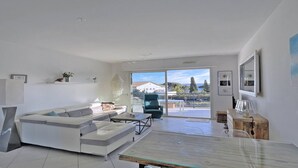 Un salon moderne avec un canapé blanc, une table basse en verre et une vue sur l’extérieur grâce à de grandes portes coulissantes.