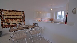 Une cuisine de taille réduite avec des meubles blancs, une table à manger en bois et une décoration murale à motifs.