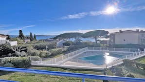 Une piscine avec vue sur la mer, entourée de verdure et délimitée par une clôture blanche.