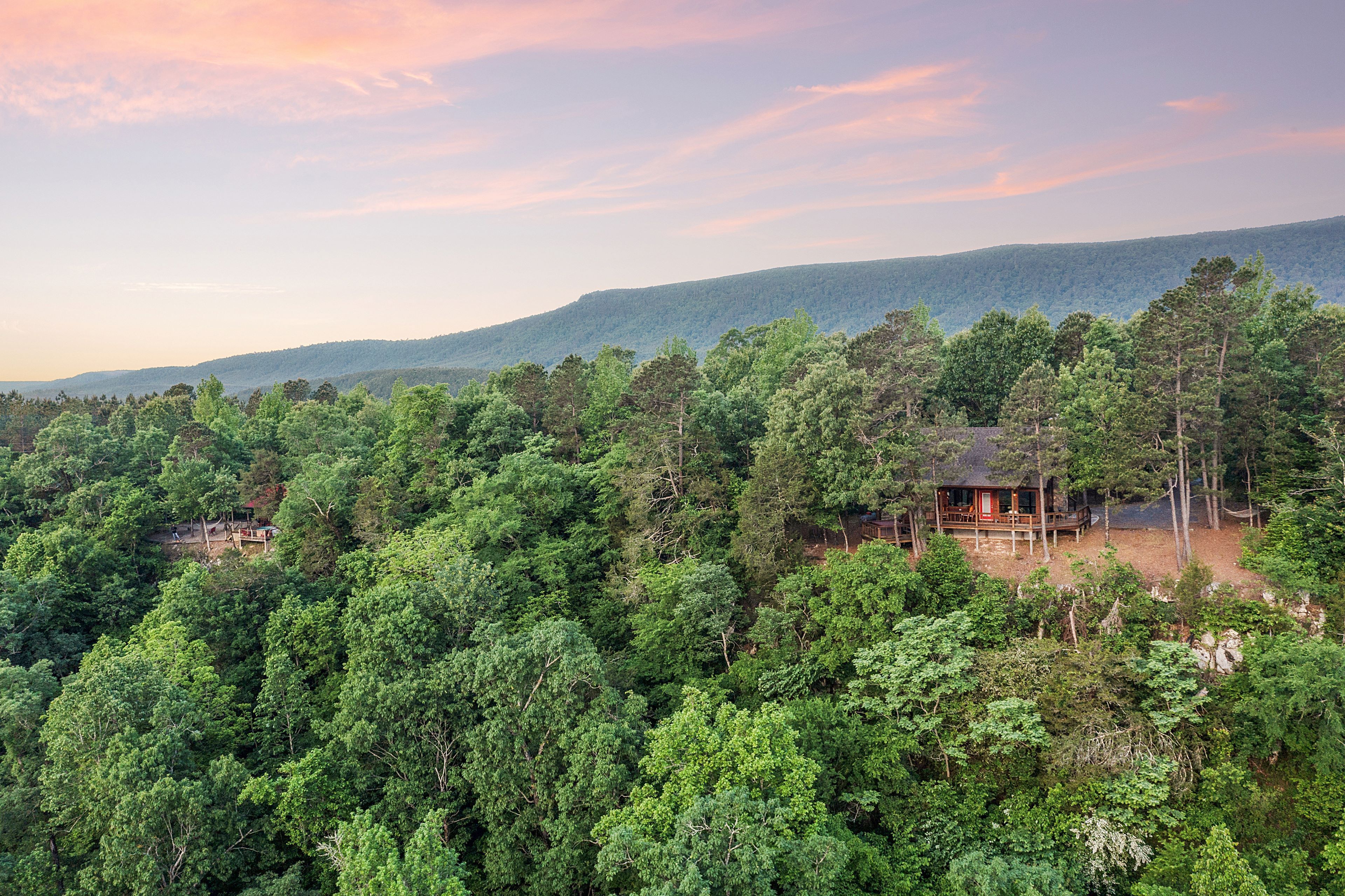 A cabin surrounded by dense forest, with a view of distant hills.
