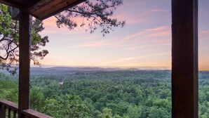 Une terrasse en bois offrant une vue sur une forêt dense et des collines lointaines.