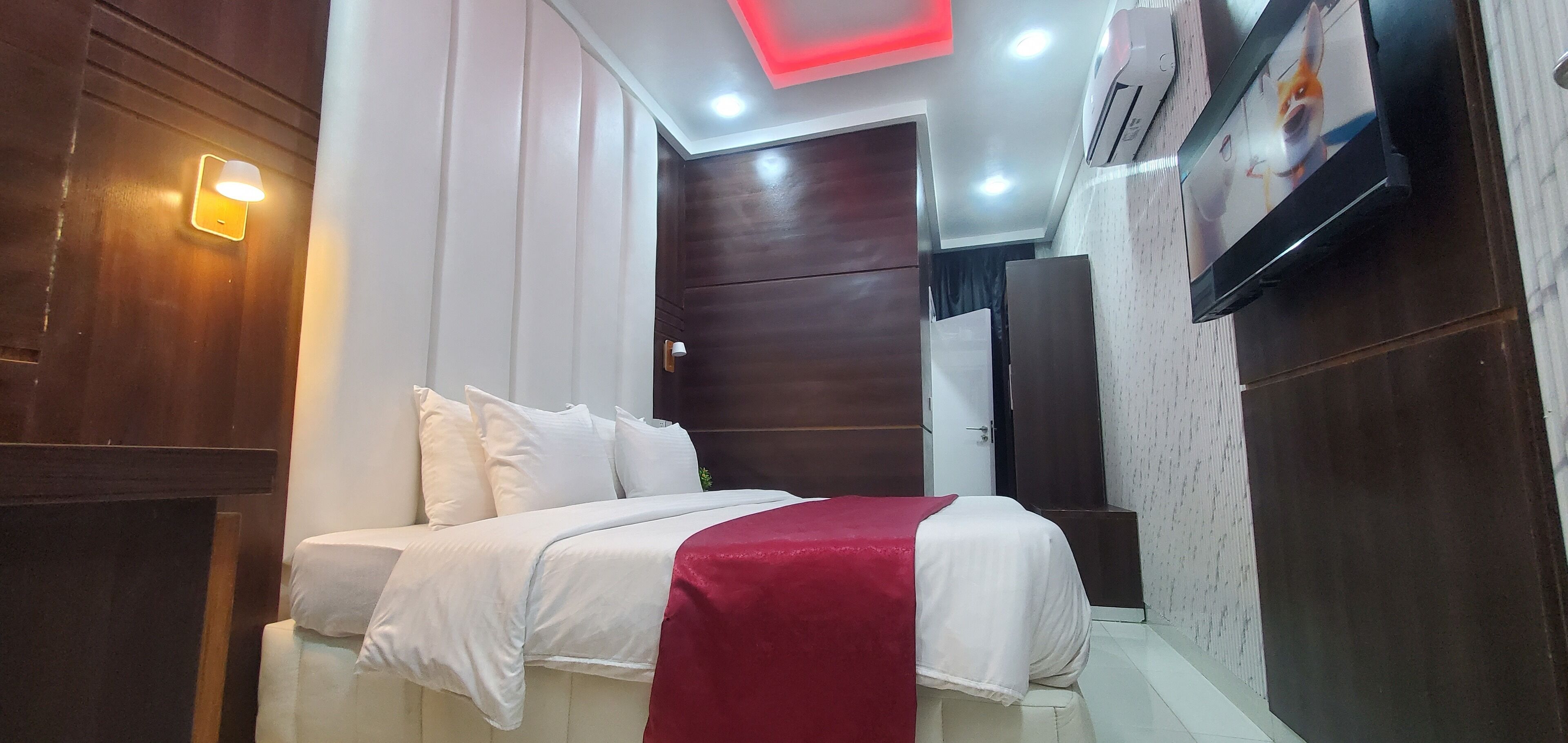A hotel room with a bed, a red throw blanket, a TV, and a wardrobe.