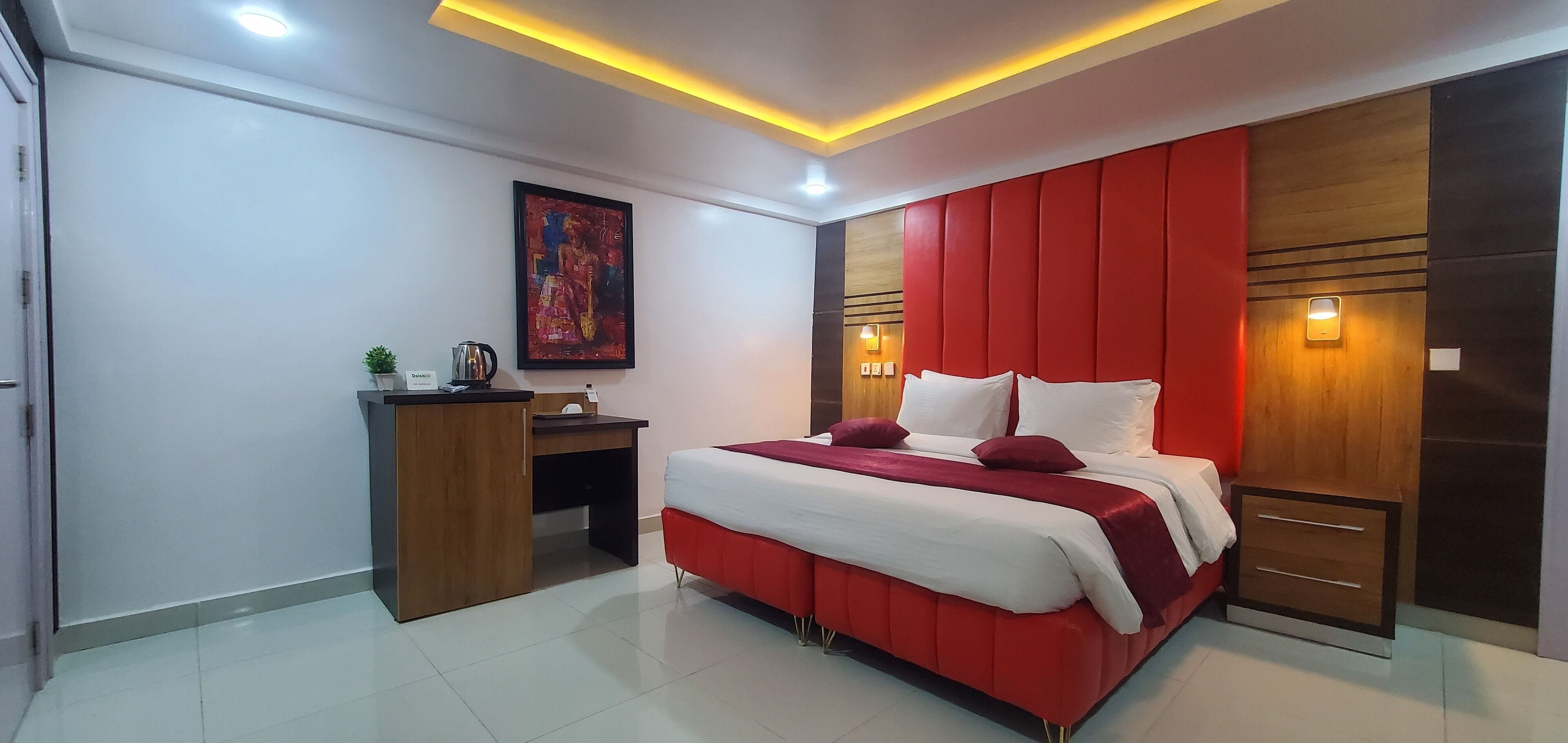 A modern bedroom with a large bed, a desk, and a red accent wall.