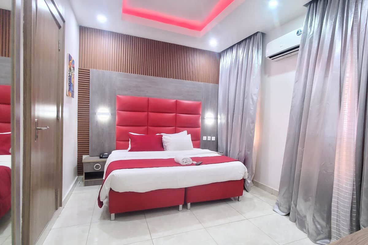A modern hotel room with a red bed, a wooden headboard, and a large mirror.
