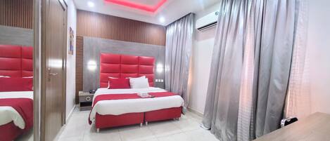 A modern hotel room with a red bed, a wooden headboard, and a large mirror.
