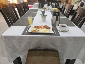 A breakfast table with a plate of toast, eggs, beans, and tomatoes, a thermos, a cup of coffee, and a glass of orange juice. - Dalchifit Suites (Abuja)