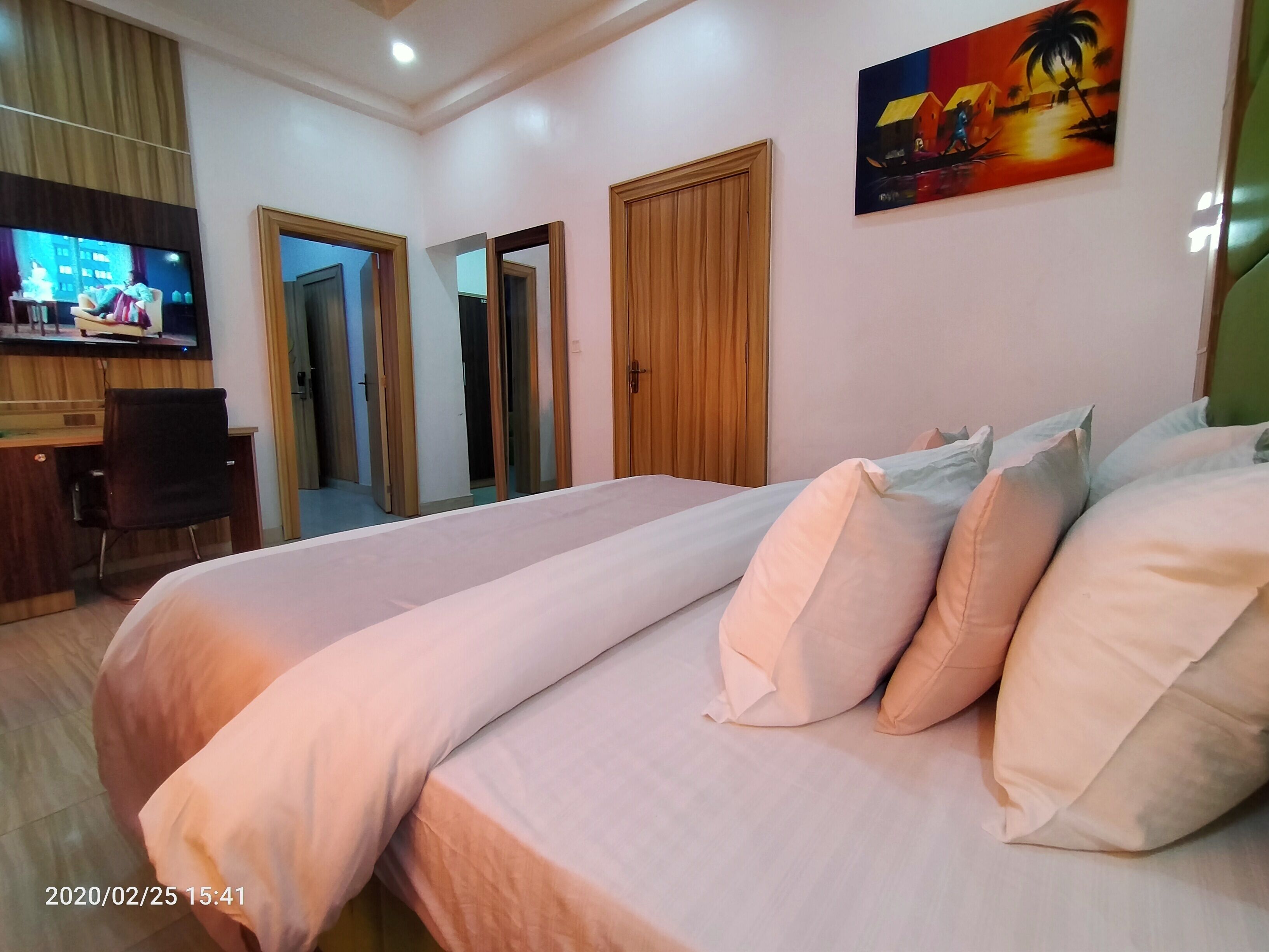A hotel room with two beds, a desk with a chair, a TV, and a painting on the wall.