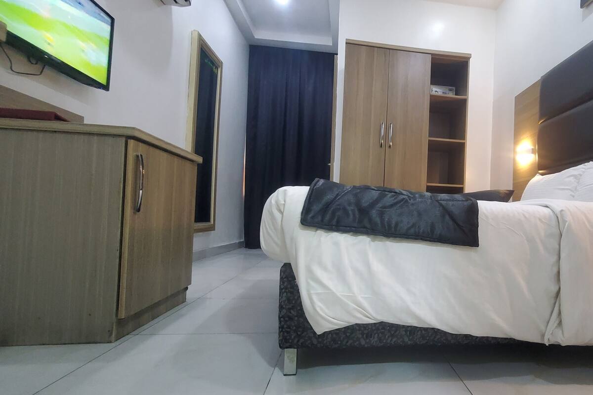 A neatly arranged hotel room with a bed, bedside table, wardrobe, and a television mounted on the wall.