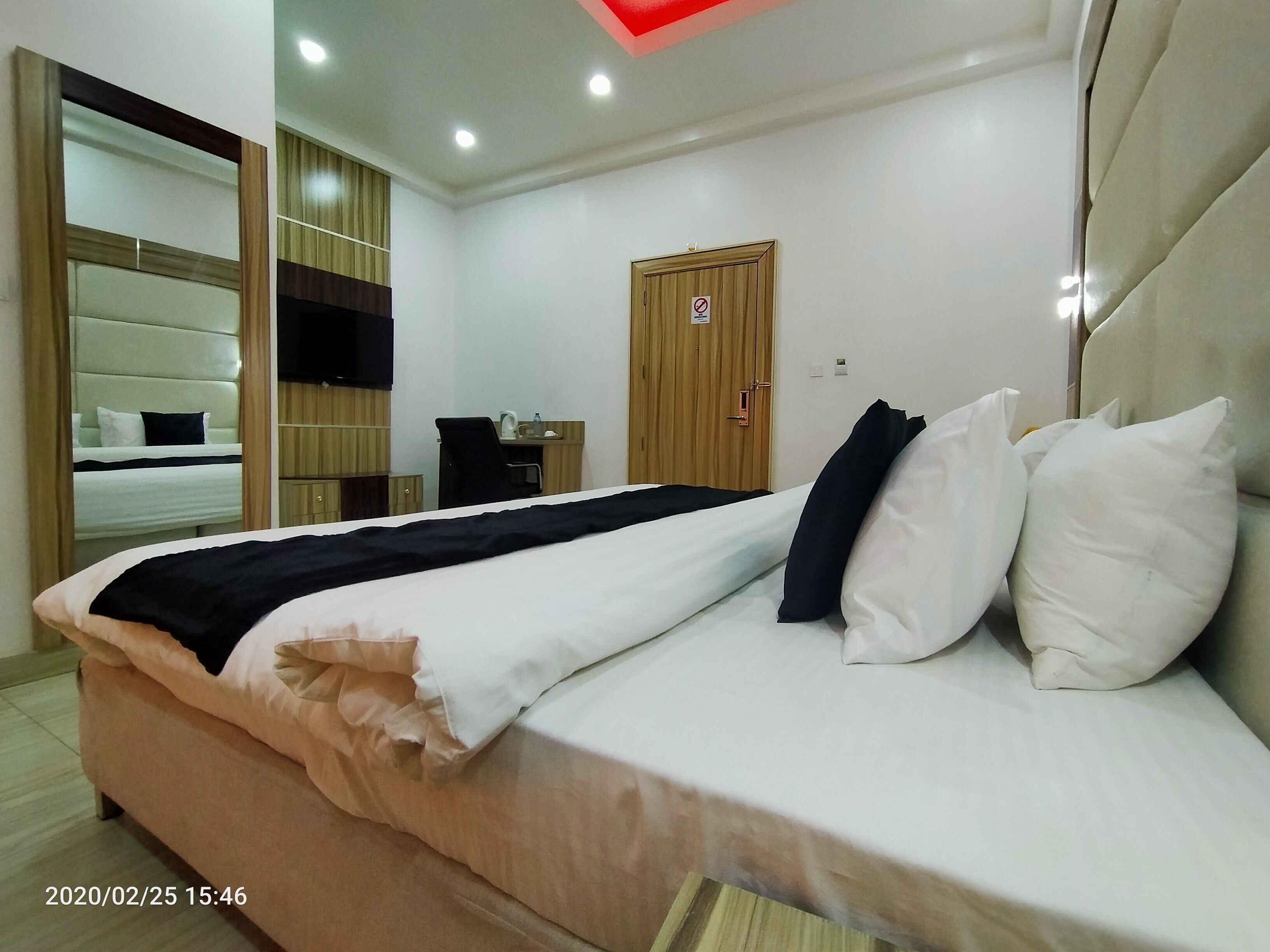 A hotel room with a bed, a desk, a wardrobe, and a door with a 'no smoking' sign.