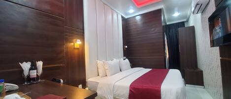 A hotel room with a bed, bedside table, and a TV mounted on the wall.