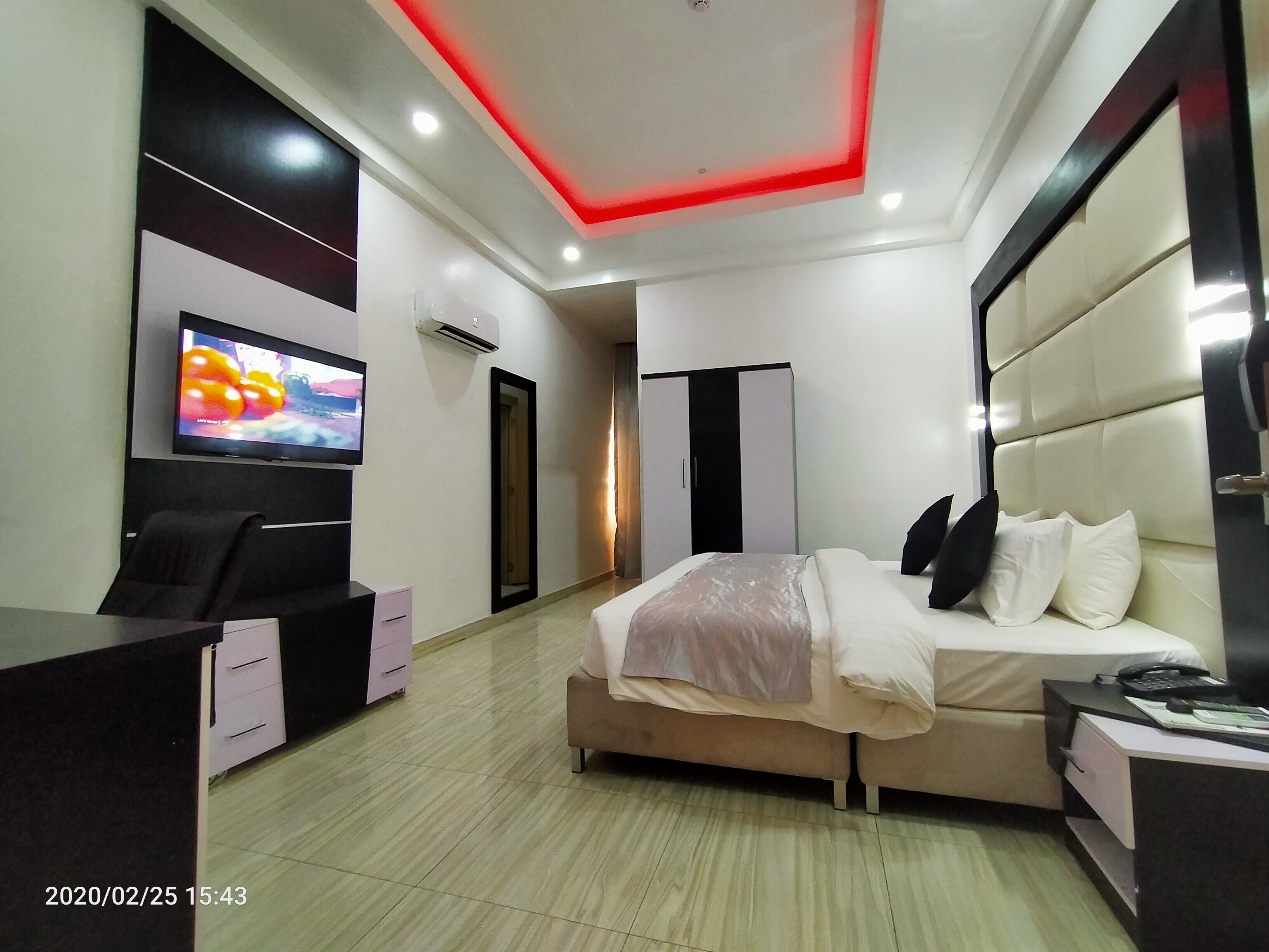 A modern hotel room with a bed, a desk, a television, and a wardrobe.