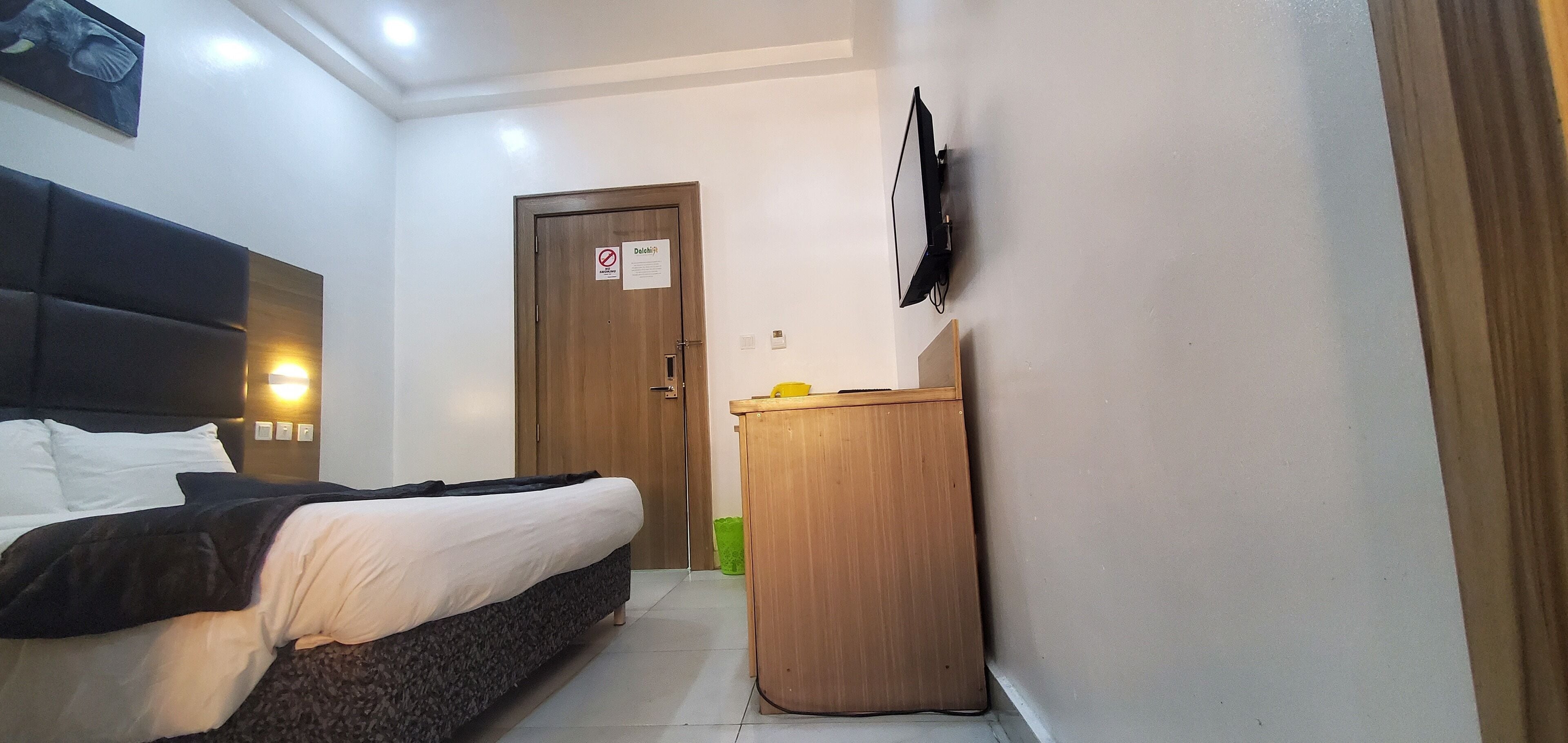 Een hotelkamer met een bed, een houten bureau, een tv aan de muur en een deur met een bordje.