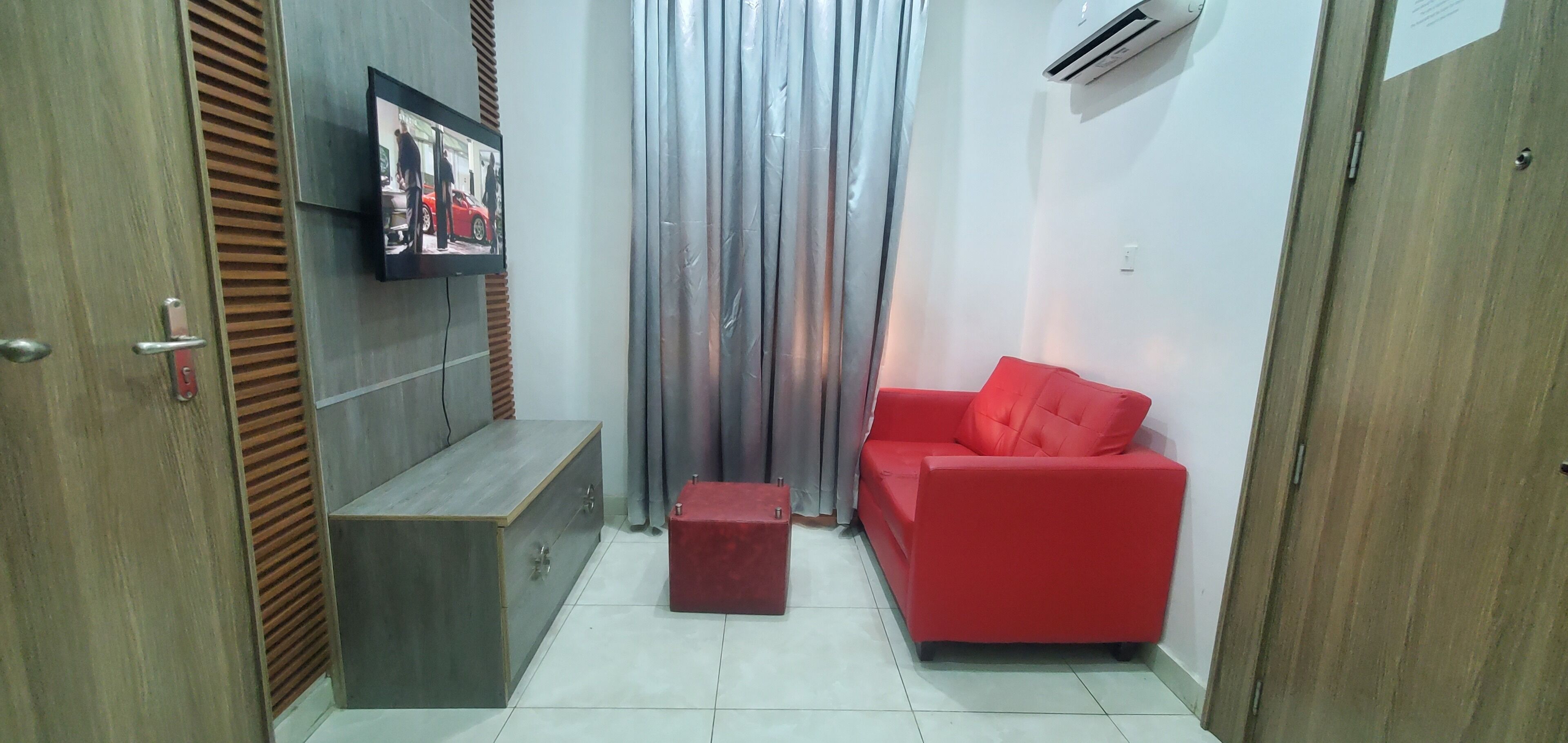 Un espace de vie compact comprenant un canapé rouge, un meuble en bois et un téléviseur fixé au mur.