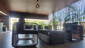 Un'area salotto interna moderna con mobili in vimini e un tavolo in vetro, affacciata su un giardino.