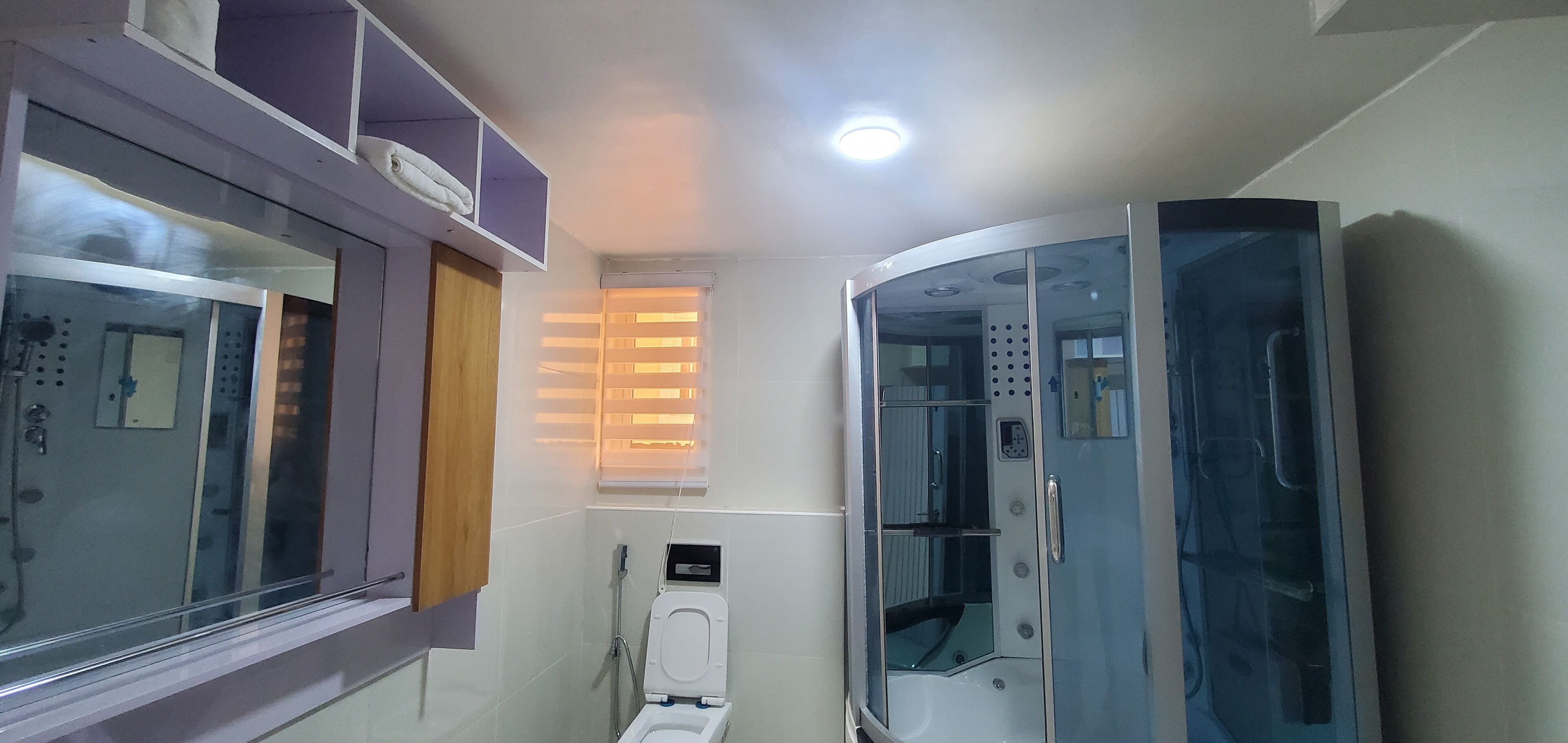 Un baño pequeño con inodoro, cabina de ducha y ventana con persianas.