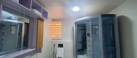 Un baño pequeño con inodoro, cabina de ducha y ventana con persianas.