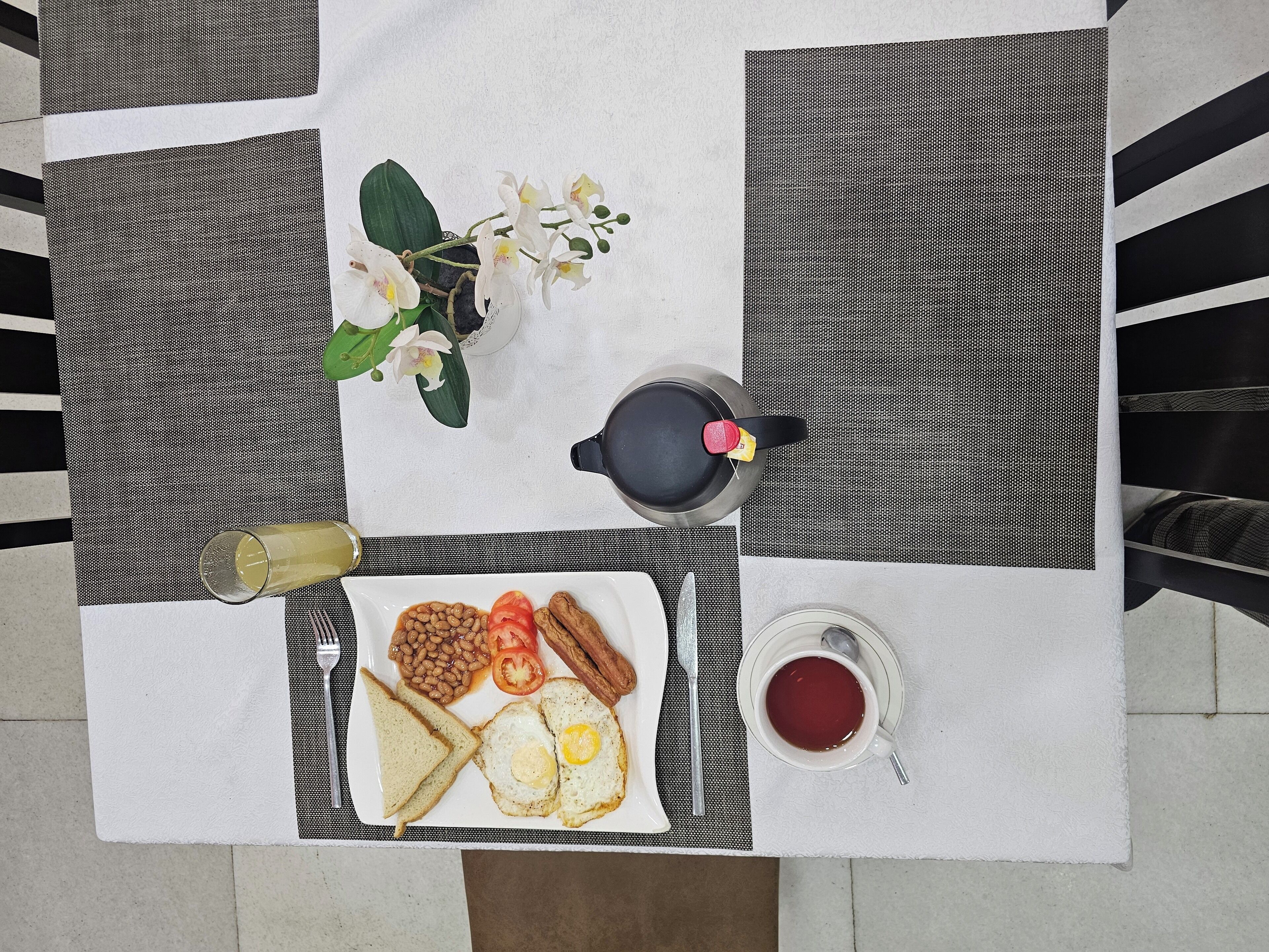 A breakfast setup with toast, eggs, beans, bacon, and a cup of tea on a table with a black and white checkered tablecloth.