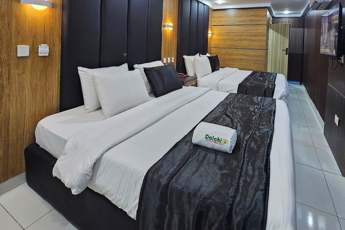 A modern hotel room with a large bed, wooden paneling, and built-in lighting.
