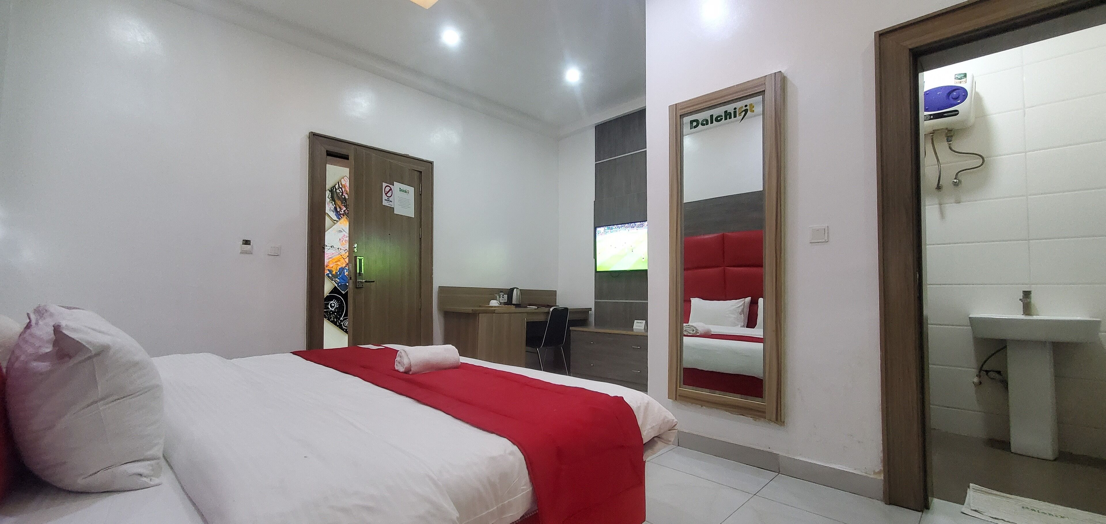 Habitación de hotel con cama, escritorio, espejo y baño con lavamanos.