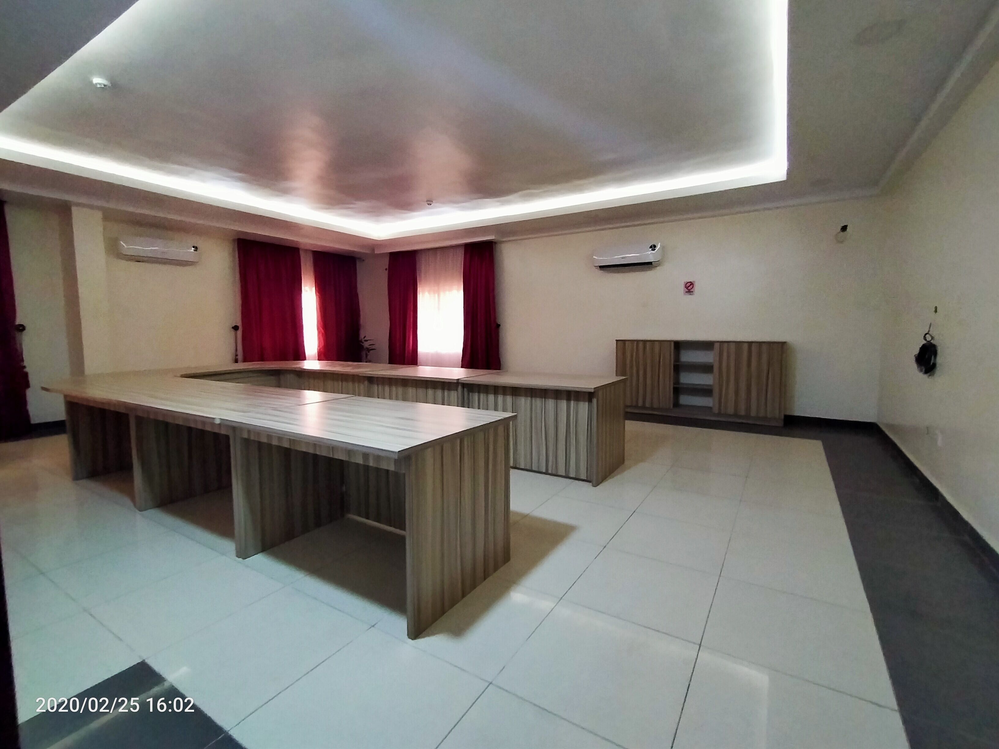 A modern room with a central wooden table, red curtains, and a ceiling light fixture.