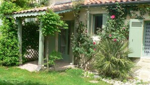 Ein Haus mit überdachter Veranda, einem kleinen Garten mit einer Palme und einer grünen Tür.