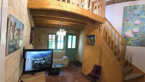 Ein gemütliches Wohnzimmer mit einer Holztreppe, einem Flachbildfernseher und Kunstwerken an den Wänden.
