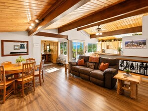 A spacious living area with a wooden ceiling, a leather sofa, a dining table with chairs, and a view of the outdoors through a sliding door.
